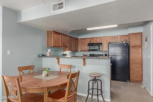 kitchen with black appliances, a breakfast bar area, light tile patterned floors, kitchen peninsula, and a textured ceiling