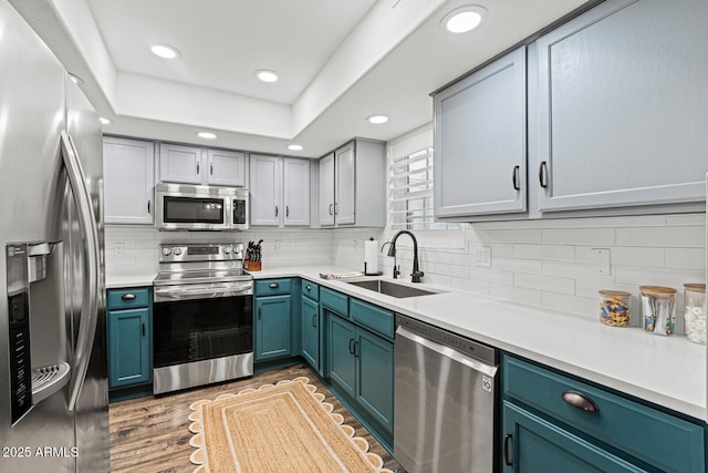 kitchen with backsplash, blue cabinets, sink, light hardwood / wood-style flooring, and appliances with stainless steel finishes