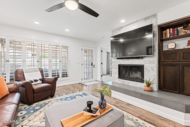 living room featuring a premium fireplace, light hardwood / wood-style flooring, and ceiling fan