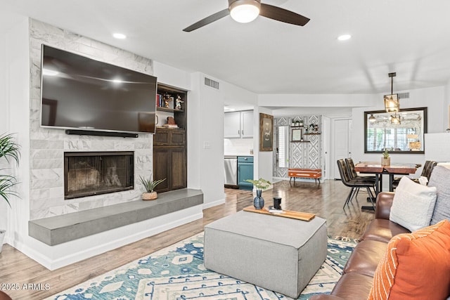 living room featuring a high end fireplace, light wood-type flooring, and ceiling fan