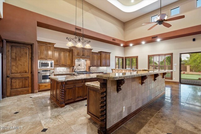 3523 E Presidio Cir, Mesa, AZ 85213 - kitchen with appliances with stainless steel finishes, a spacious island, brown cabinets, a ceiling fan, and a breakfast bar
