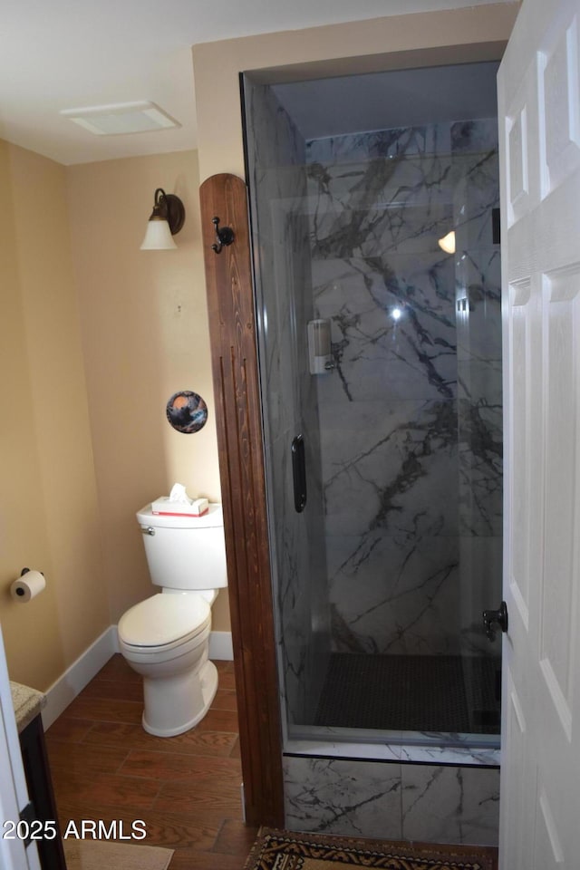 bathroom with a marble finish shower, toilet, baseboards, and wood finished floors