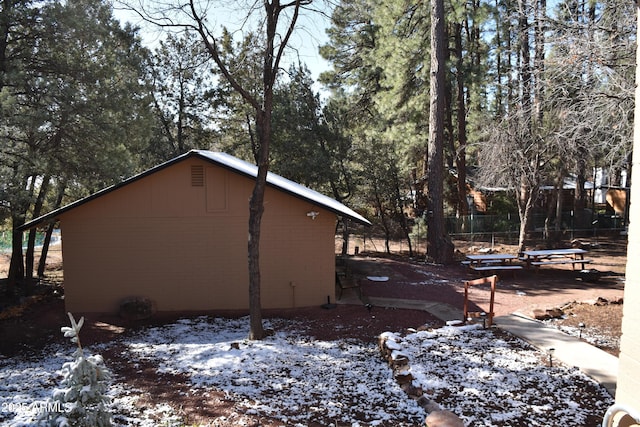 view of snowy exterior with brick siding and fence