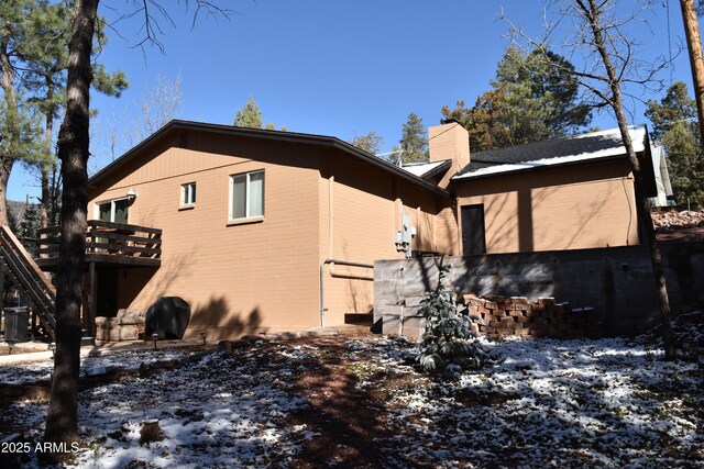 snow covered property with a wooden deck, brick siding, and a chimney