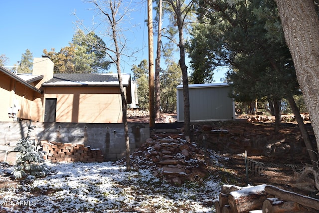 view of snow covered exterior featuring a shingled roof, an outbuilding, fence, and a chimney