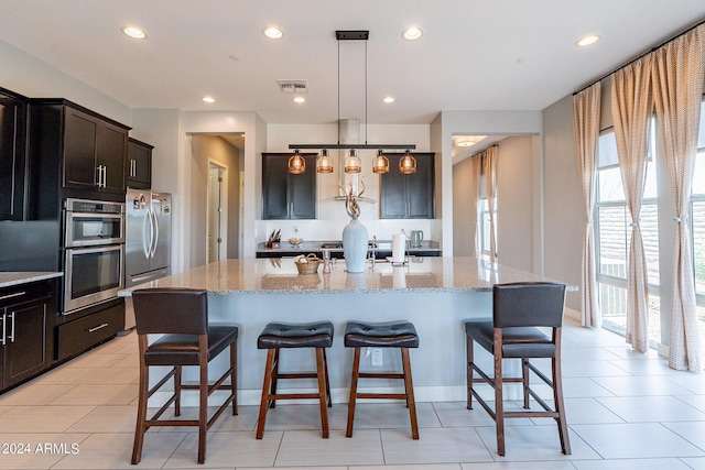 kitchen featuring decorative light fixtures, light stone countertops, an island with sink, and appliances with stainless steel finishes