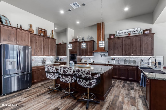 kitchen with light stone counters, a kitchen island, dark wood-type flooring, wall chimney exhaust hood, and stainless steel appliances