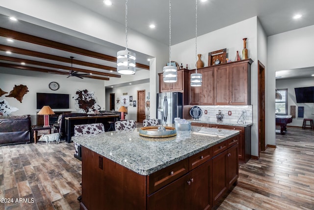 kitchen with a kitchen island, black fridge, hanging light fixtures, light stone counters, and dark hardwood / wood-style flooring