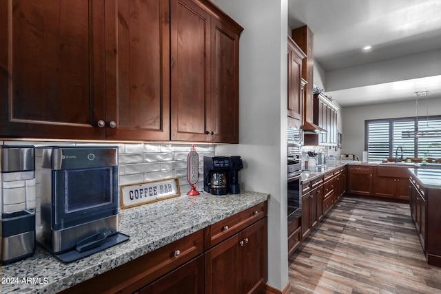 kitchen with stainless steel oven, wood-type flooring, backsplash, sink, and light stone counters