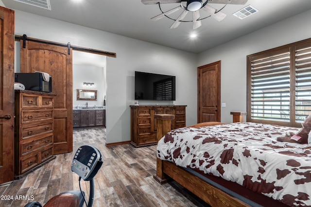 bedroom featuring connected bathroom, ceiling fan, a barn door, and hardwood / wood-style floors