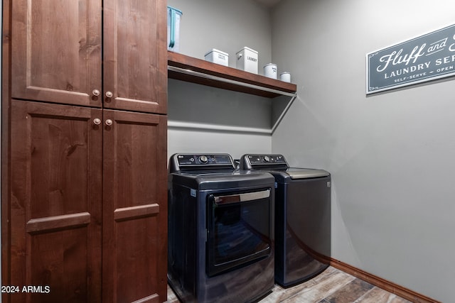 clothes washing area featuring cabinets, washer and clothes dryer, and light hardwood / wood-style floors