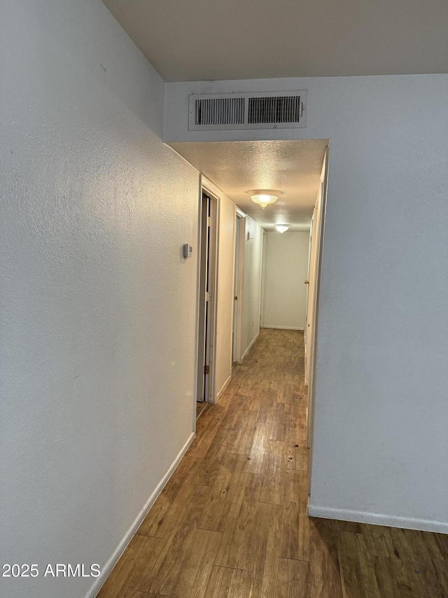 hall with visible vents, baseboards, and wood finished floors