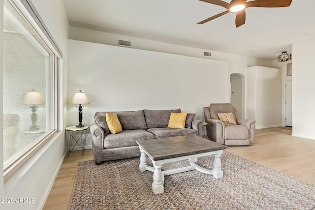 living room with light wood finished floors, visible vents, arched walkways, baseboards, and a ceiling fan