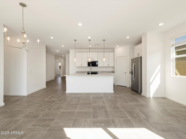 kitchen with pendant lighting, light countertops, white cabinets, an island with sink, and stainless steel fridge