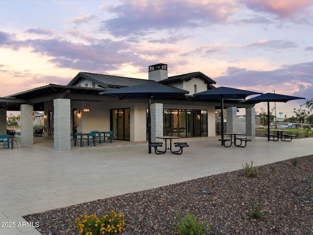 back of property at dusk with a chimney, a patio area, and stucco siding