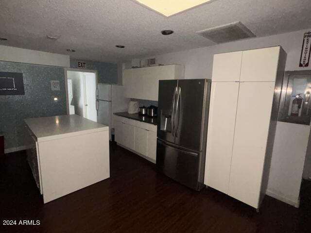 kitchen with white refrigerator, white cabinetry, a kitchen island, and stainless steel fridge