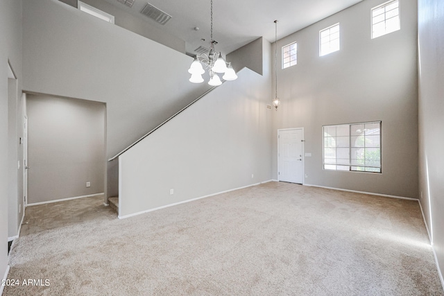 unfurnished living room with carpet, plenty of natural light, an inviting chandelier, and a towering ceiling