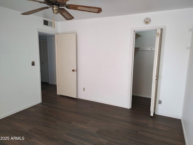 unfurnished bedroom featuring a spacious closet, dark wood-type flooring, a closet, and ceiling fan