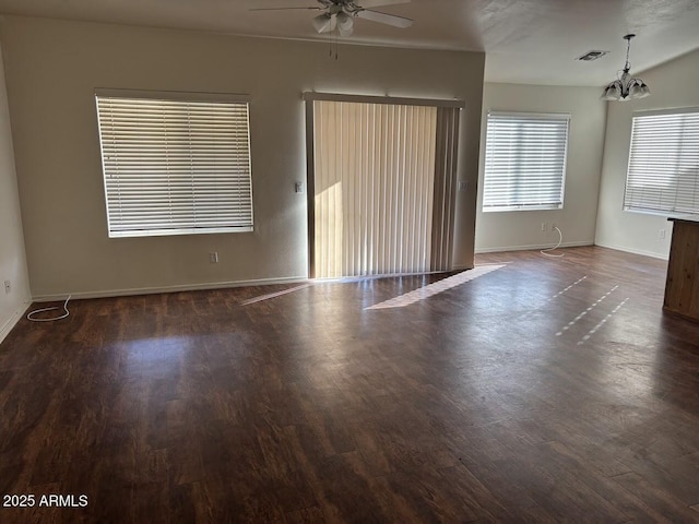 empty room with ceiling fan with notable chandelier, dark wood-style flooring, visible vents, and baseboards