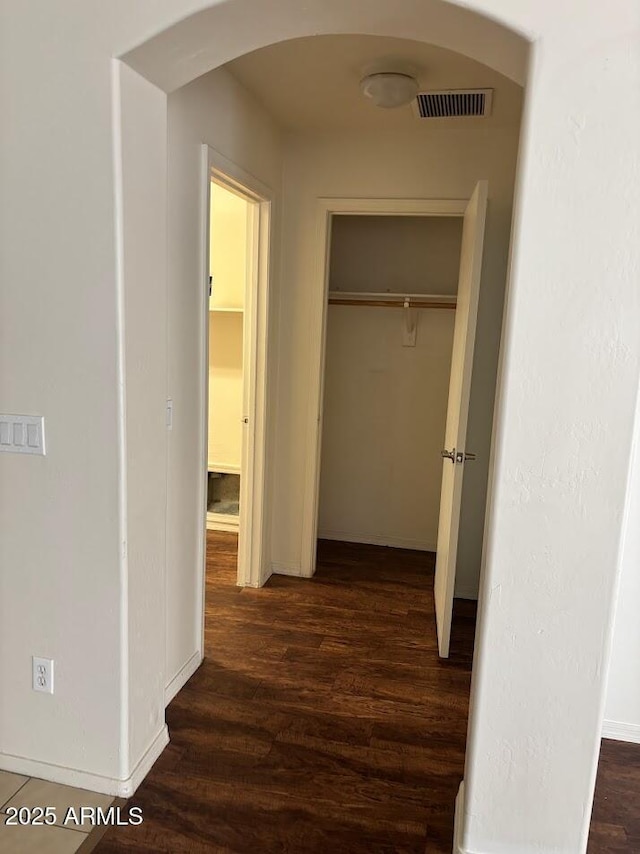 hallway featuring arched walkways, visible vents, dark wood finished floors, and baseboards