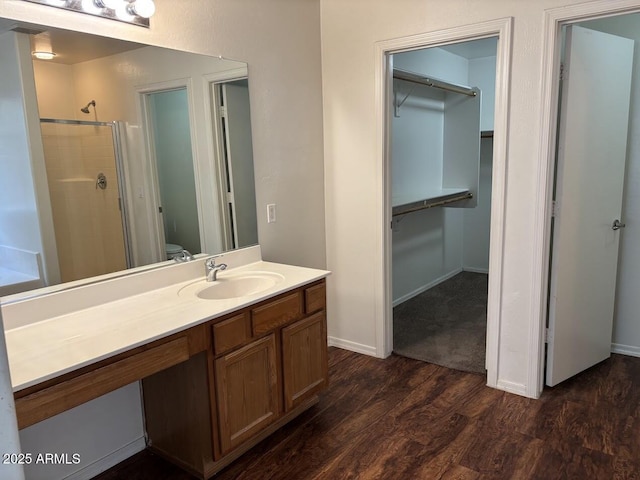 full bath with a stall shower, baseboards, wood finished floors, a walk in closet, and vanity