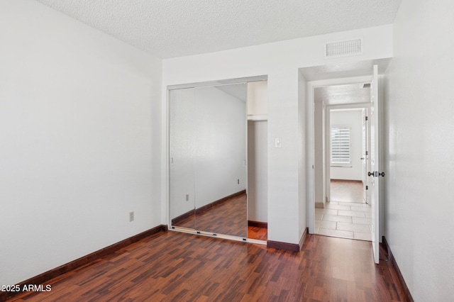 unfurnished bedroom with dark wood-type flooring, a textured ceiling, and a closet