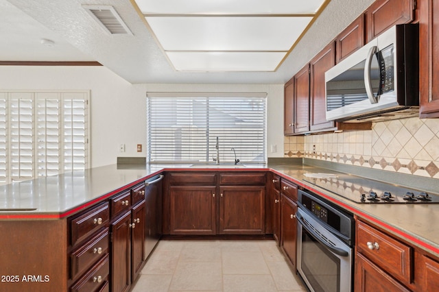 kitchen with appliances with stainless steel finishes, kitchen peninsula, sink, light tile patterned flooring, and tasteful backsplash