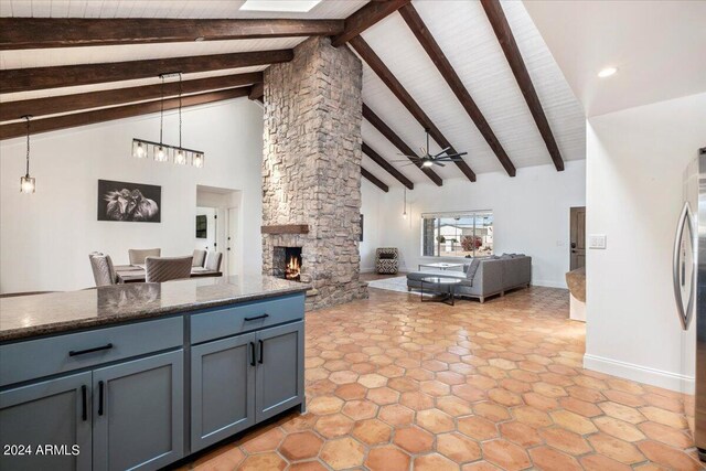 kitchen featuring ceiling fan, a stone fireplace, high vaulted ceiling, decorative light fixtures, and beamed ceiling