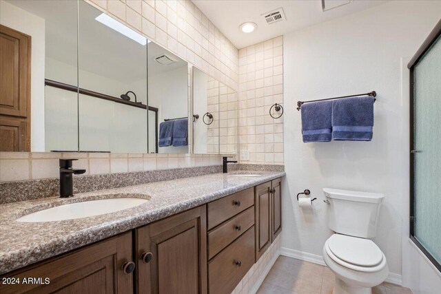 full bathroom featuring dual bowl vanity, tasteful backsplash, tile patterned flooring, tile walls, and toilet