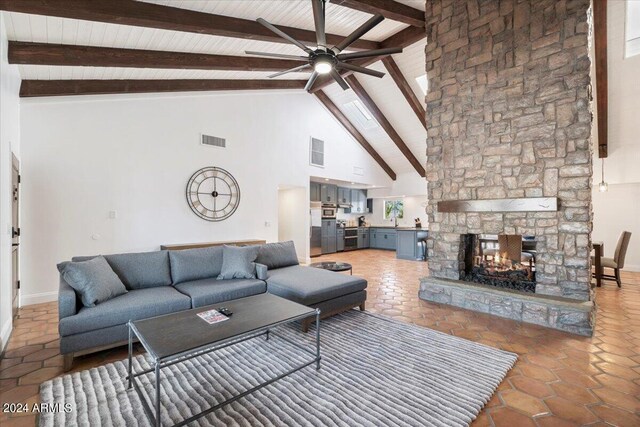 living room with high vaulted ceiling, a fireplace, beamed ceiling, dark tile patterned floors, and ceiling fan