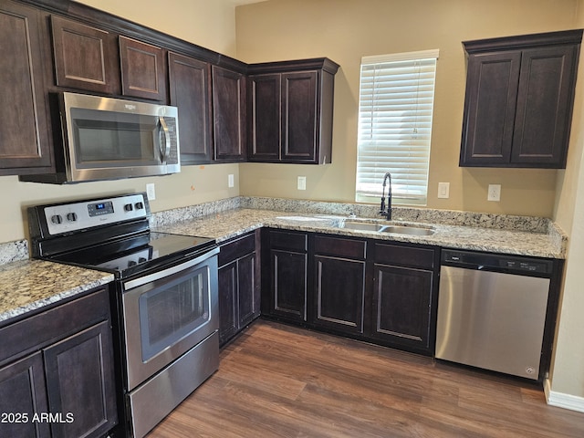 kitchen featuring dark wood finished floors, dark brown cabinetry, light stone counters, stainless steel appliances, and a sink
