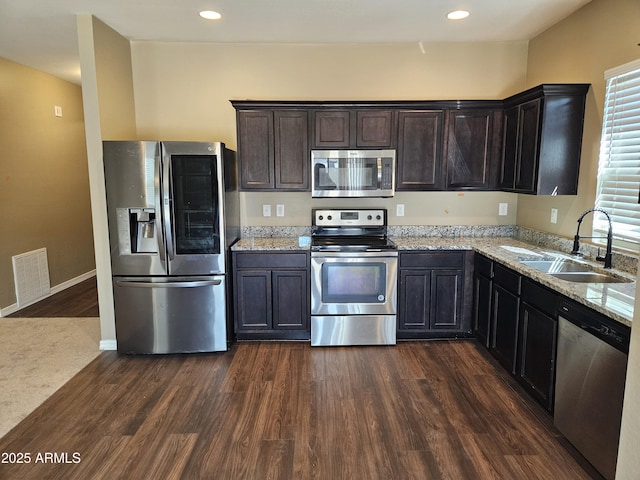 kitchen with visible vents, a sink, light stone counters, appliances with stainless steel finishes, and dark wood-style flooring