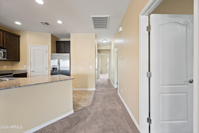 kitchen featuring dark brown cabinetry, light stone countertops, light carpet, and stainless steel appliances