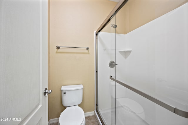 bathroom featuring a shower with door and toilet