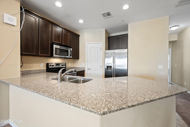 kitchen with kitchen peninsula, light stone countertops, stainless steel appliances, dark brown cabinets, and sink