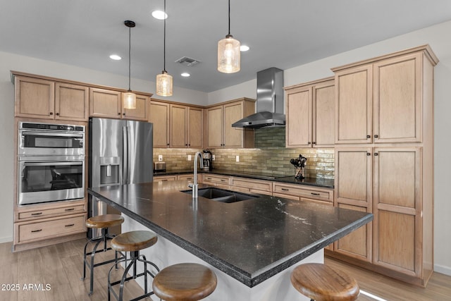 kitchen with stainless steel appliances, a breakfast bar, a sink, visible vents, and wall chimney exhaust hood