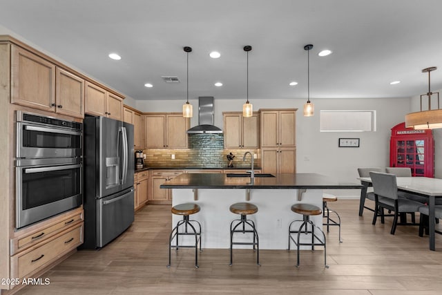 kitchen featuring visible vents, dark countertops, wall chimney exhaust hood, stainless steel appliances, and a sink