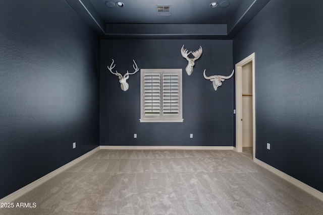 carpeted spare room featuring a tray ceiling, baseboards, and visible vents