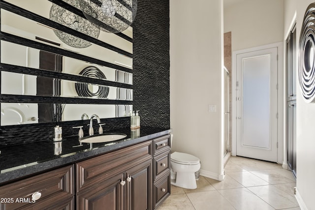 bathroom with baseboards, toilet, tile patterned flooring, vanity, and a stall shower