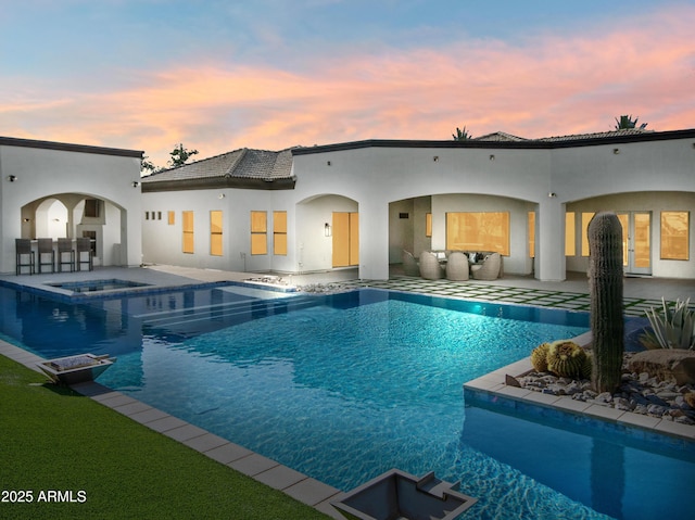 rear view of house featuring a tiled roof, a pool with connected hot tub, an outdoor living space, a patio, and stucco siding