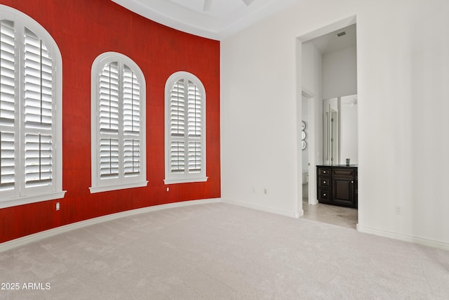 unfurnished bedroom featuring carpet, an accent wall, baseboards, and ensuite bath