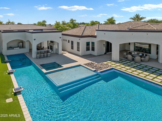 back of property featuring a pool with connected hot tub, outdoor wet bar, stucco siding, a patio area, and a tile roof
