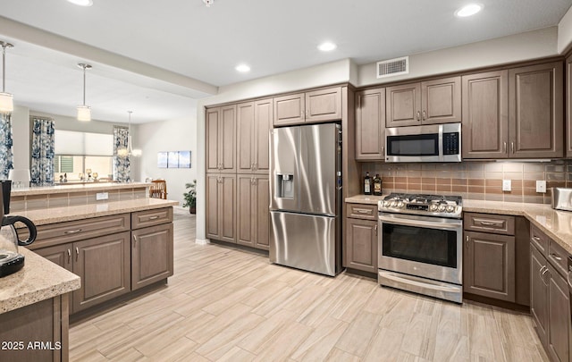 kitchen with decorative backsplash, light stone countertops, recessed lighting, appliances with stainless steel finishes, and decorative light fixtures