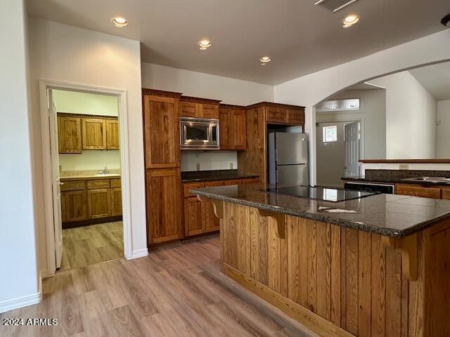 kitchen with a breakfast bar area, a large island, stainless steel appliances, dark stone counters, and hardwood / wood-style floors