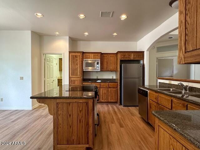 kitchen with light hardwood / wood-style flooring, a kitchen island, dark stone countertops, stainless steel appliances, and sink