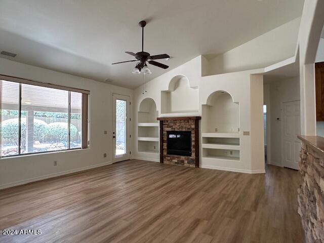 unfurnished living room featuring a fireplace, lofted ceiling, built in shelves, hardwood / wood-style flooring, and ceiling fan