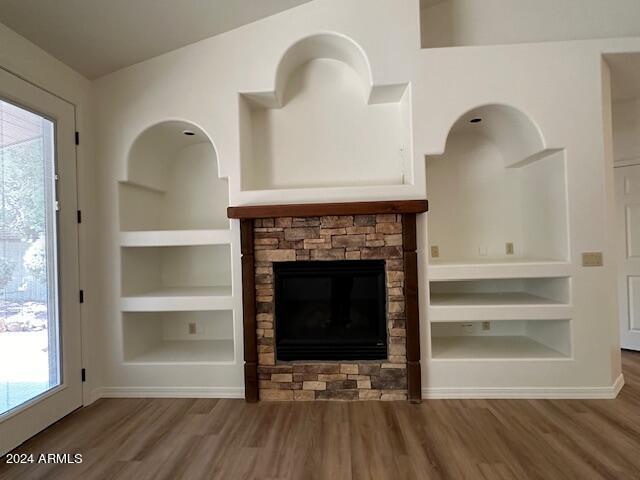 unfurnished living room featuring built in features, a stone fireplace, plenty of natural light, and hardwood / wood-style floors