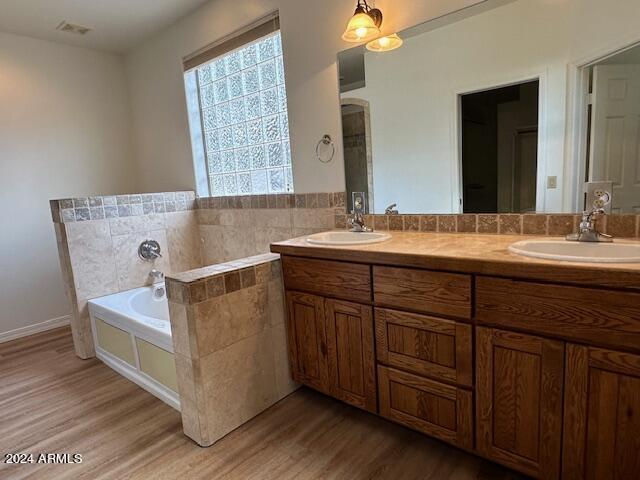 bathroom with double vanity, hardwood / wood-style floors, a bath, and a healthy amount of sunlight