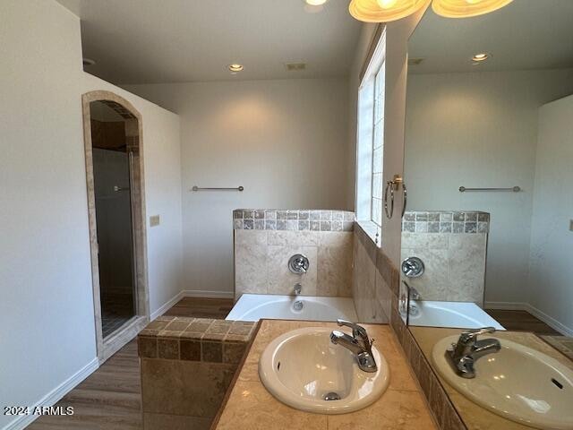 bathroom featuring dual bowl vanity, hardwood / wood-style flooring, and independent shower and bath