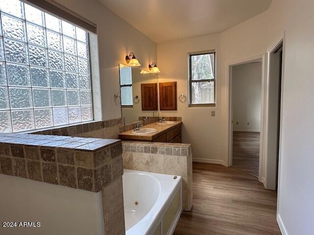 bathroom with dual bowl vanity, hardwood / wood-style floors, and tiled bath